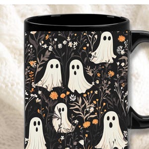 May include: Black coffee mug with a white ghost and floral pattern. The mug has a black handle and a black rim.