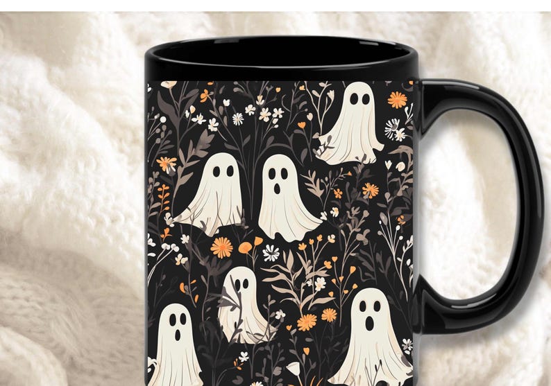 May include: Black coffee mug with a white ghost and floral pattern. The mug has a black handle and a black rim.