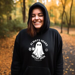 May include: Black hooded sweatshirt with a white ghost graphic and the text "Always Heard Never Seen Dispatch". The ghost is holding a cup of coffee and there are police and fire department badges on either side of the ghost.