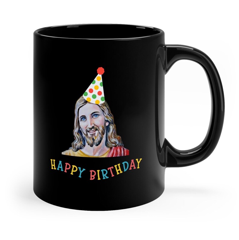 Puede incluir: Taza de caf&eacute; negra con una imagen blanca de Jes&uacute;s usando un gorro de fiesta colorido. El texto "Happy Birthday" est&aacute; impreso en colores arco&iacute;ris debajo de la imagen.