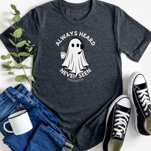 May include: A dark gray t-shirt with a white ghost graphic and the text "Always Heard Never Seen Dispatch".