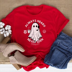 May include: Red t-shirt with a white ghost graphic and the text "Always Heard Never Seen Dispatch". The ghost is wearing a headset and holding a cup of coffee.