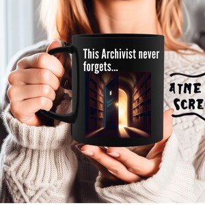 Könnte beinhalten: Schwarze Kaffeetasse mit weißem Design. Das Design zeigt eine Bibliothek mit einer offenen Tür, die ein helles Licht freigibt. Der Text auf der Tasse lautet "This Archivist never forgets..."