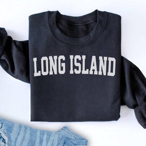 Può includere: Una felpa nera a maniche lunghe con la scritta "LONG ISLAND" stampata in bianco sul davanti.