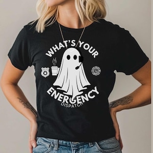May include: Black t-shirt with a white ghost wearing a headset and holding a coffee cup. The text "What's Your Emergency Dispatch" is printed on the shirt.