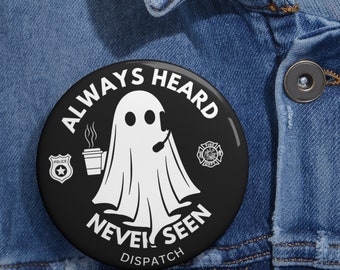May include: Black and white button with a ghost holding a cup of coffee and a headset. The text on the button reads "Always Heard Never Seen Dispatch".