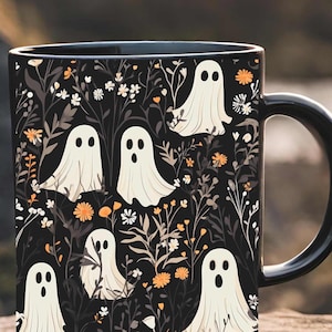 May include: Black coffee mug with a white ghost pattern on a black background. The ghosts are surrounded by white flowers and orange and yellow flowers. The mug has a black handle.