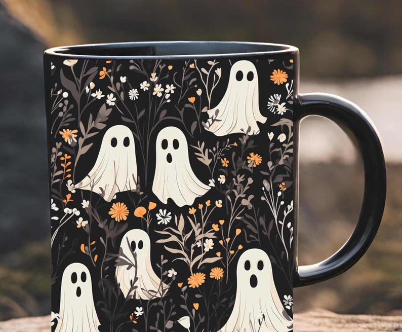 May include: Black coffee mug with a white ghost pattern on a black background. The ghosts are surrounded by white flowers and orange and yellow flowers. The mug has a black handle.