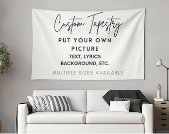 Op de afbeelding: Witte op maat gemaakte wandtapijt met zwarte tekst: "Custom Tapestry, PUT YOUR OWN PICTURE, TEXT, LYRICS, BACKGROUND, ETC., MULTIPLE SIZES AVAILABLE." Het wandtapijt hangt boven een witte bank met kussens.