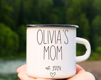 May include: White enamel mug with black trim and the text "Olivia's Mom est. 2024" with a heart.