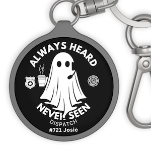 May include: A black and white ghost with a headset and coffee cup, on a black circle with the text "Always Heard Never Seen Dispatch #721 Josie" in white. The circle is attached to a silver keychain.