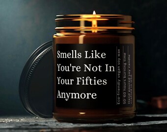 May include: A brown glass candle jar with a black label that reads "Smells Like You're Not In Your Fifties Anymore". The candle is made with eco-friendly vegan soy wax and has a burn time of 50-60 hours. It is hand-poured and crafted in the USA.