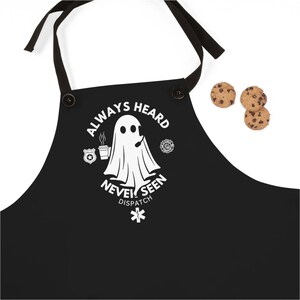 May include: Black apron with a white ghost design and the text "Always Heard Never Seen Dispatch". The ghost is holding a cup of coffee and a microphone.