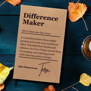 Puede incluir: Un diario de cuero marrón con las palabras "Difference Maker" en letras negras. El diario también incluye la definición de la palabra "Difference Maker" y el texto "Also known as: Jara".