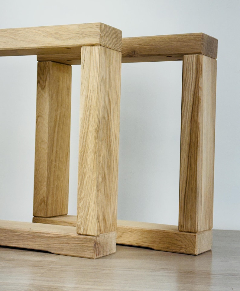 May include: Two rectangular furniture legs constructed from light-colored natural wood with a visible grain pattern. Each leg features a sturdy frame design with two vertical posts connected by a horizontal base and a top support beam.
