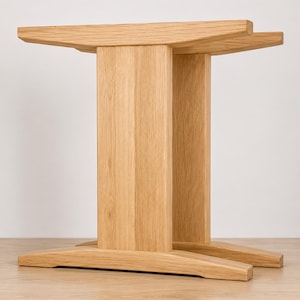 Könnte beinhalten: Ein heller Holztischfuß bestehend aus zwei vertikalen Stützsäulen, die durch ein horizontales Oberteil und zwei parallele Füße an der Basis verbunden sind. Die Struktur ist aus natürlichem Eichenholz mit sichtbarer Maserung gefertigt.
