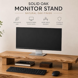 Può includere: Un supporto per monitor in rovere massello con finitura in legno naturale e dettagli a bordo vivo. Il supporto è rialzato da due gambe rettangolari in legno e sostiene un monitor per computer nero, con tastiera e mouse posizionati sulla scrivania.