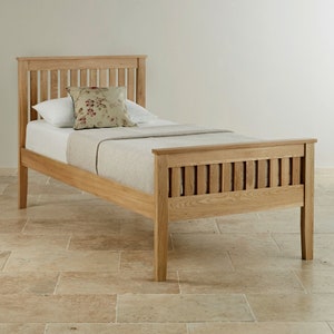 May include: A single bed frame constructed from light-colored wood with a slatted headboard and footboard. The bed is dressed with a white mattress, a beige textured blanket, and a decorative throw pillow featuring a floral pattern.