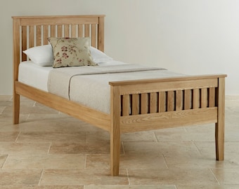 Può includere: Una struttura per letto singolo in legno chiaro con testiera e pediera a doghe. Il letto è completato da un materasso bianco, una coperta beige testurizzata e un cuscino decorativo con un motivo floreale.