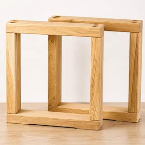 May include: Two rectangular furniture legs crafted from light-colored natural wood with a visible grain pattern. Each leg features a sturdy frame construction with four pre-drilled circular holes on the top horizontal bar for mounting purposes.