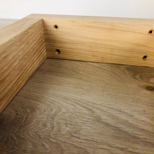 May include: A light-colored wooden frame with a natural grain pattern, featuring four pre-drilled circular holes along the inner side panel. The structure is constructed from solid wood planks joined at a right angle, showcasing a smooth finish.
