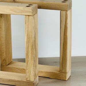 May include: Two rectangular furniture legs crafted from light-colored natural wood with a visible grain pattern. Each leg features a sturdy frame construction with two vertical posts connected by a horizontal base and a top support bar with pre-drilled holes.