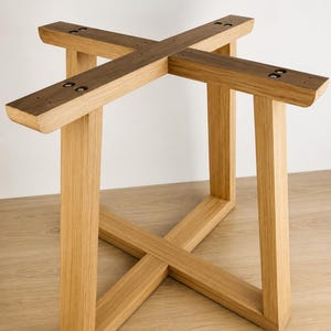 Puede incluir: Una base de mesa de madera de color claro que presenta una estructura de soporte en forma de cruz en la parte inferior y un marco superior a juego en forma de cruz. El diseño consta de cuatro patas verticales conectadas por vigas horizontales con acabado de veta natural.