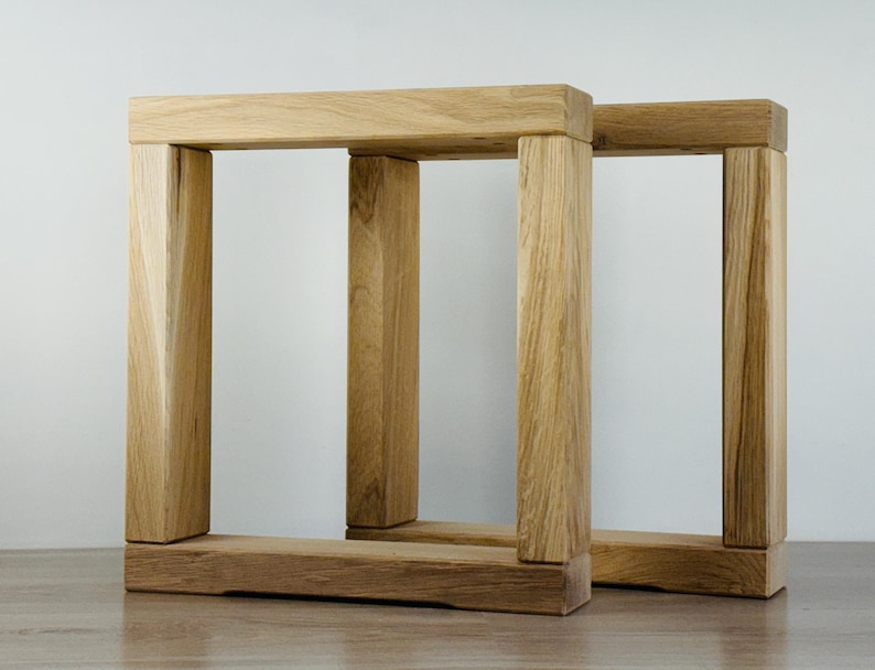 May include: Two rectangular table legs constructed from light-colored natural wood with a visible grain pattern. Each leg features a sturdy base, two vertical supports, and a horizontal top beam, forming a clean, open, and geometric frame structure.