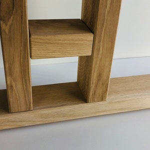 May include: A light brown oak wood furniture base featuring two vertical support beams connected by a horizontal block, all attached to a long, flat rectangular base plate with a visible wood grain texture and natural light tan color tones.