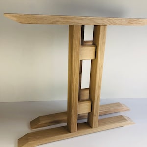 May include: A wooden table base with a unique, open design. The base is made of light brown wood and has a rectangular top with two legs that extend out to the sides. The legs are connected by a series of horizontal and vertical supports.