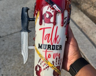 May include: A white glitter tumbler featuring a red blood drip effect, red handprints, and a yellow crime scene tape graphic. The text reads Talk MURDER to me. It includes a black and silver knife handle as the cup handle and a small knife charm.