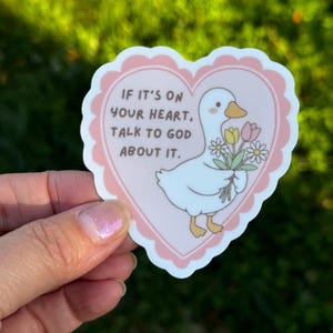 May include: A sticker featuring a white goose holding flowers inside a pink heart with a scalloped edge. The text reads, "If it's on your heart, talk to God about it."