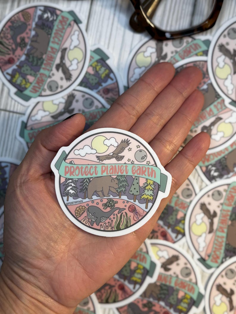 May include: A round sticker with a pink background and a green banner that says "protect planet earth". The sticker features a variety of animals and plants, including a bear, a whale, a turtle, a bird, and trees. The sticker is designed to promote environmental awareness.