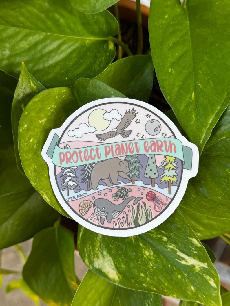 May include: A round sticker with a pink background and a white border. The sticker features a colorful illustration of a bear, a whale, a turtle, a bird, a moon, and a sun. The text "Protect Planet Earth" is written in a banner across the top of the sticker.