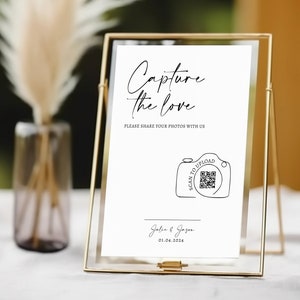 May include: A gold framed sign with the words "Capture the love" in script. The sign includes the text "PLEASE SHARE YOUR PHOTOS WITH US" and a QR code with a camera graphic. The date "01.04.2024" is also displayed.