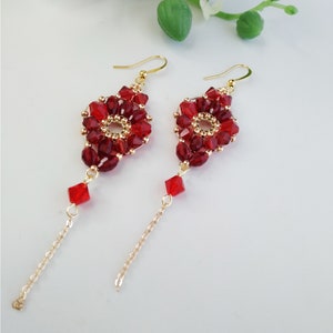 Peut inclure: Une paire de boucles d'oreilles longues et pendantes avec un motif de perles rouges. Les boucles d'oreilles présentent une chaîne dorée avec une perle de cristal rouge au bas.