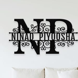 May include: Black metal wall art displaying the intertwined letters "ND" and the names "NINAD PIYOOSHA" below. The design incorporates decorative scrollwork. It is mounted above a white sofa with cushions.