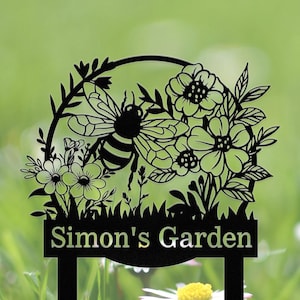 May include: Black metal garden sign featuring a bee and floral design. The sign reads "Simon's Garden".