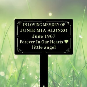 Könnte beinhalten: Ein schwarzer, rechteckiger Gedenk-Gartenstecker mit spitzem Ende. Der Text lautet: IN LOVING MEMORY OF JUNIE MIA ALONZO, June 1967, Forever In Our Hearts und little angel, ergänzt durch ein kleines Herzsymbol und dekorative Verzierungen.