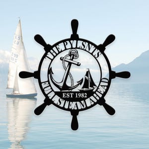 Puede incluir: Arte de pared de rueda de barco de metal negro con el texto "THE PYLSNTS FULL STEAM AHEAD EST 1982". El diseño incluye un ancla, una cuerda y un velero. Un velero está en el fondo.
