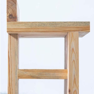 May include: A handcrafted wooden chair with a simple, modern design. The chair is constructed from light-colored wood, featuring a rectangular seat, four sturdy legs, and a small backrest. The natural wood grain is visible, adding to its rustic charm.