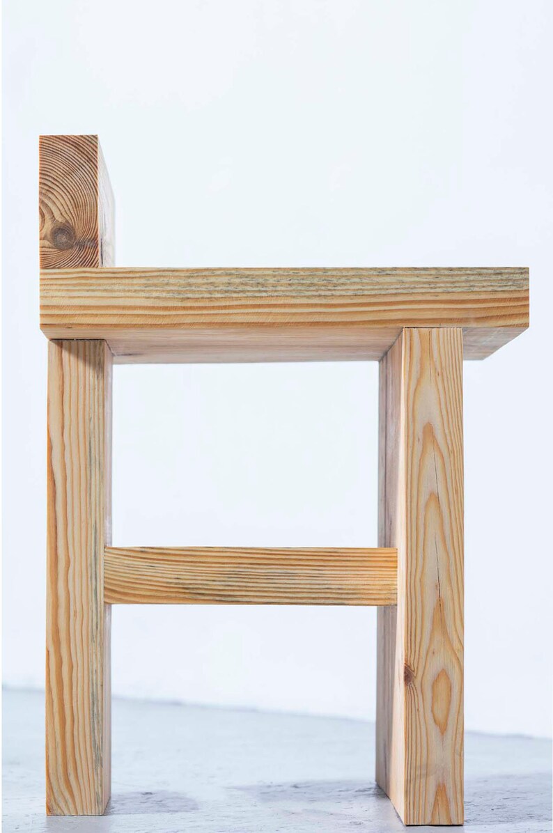 May include: A handcrafted wooden chair with a simple, modern design. The chair is constructed from light-colored wood, featuring a rectangular seat, four sturdy legs, and a small backrest. The natural wood grain is visible, adding to its rustic charm.