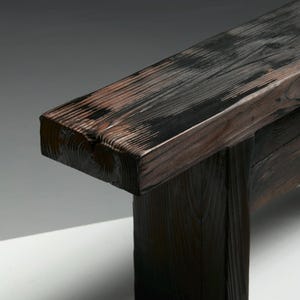 May include: A dark brown wooden bench with a rectangular seat and thick, square legs. The wood grain is visible, with a mix of dark and lighter brown tones. The bench appears to be sturdy and well-crafted, suitable for indoor or outdoor use.