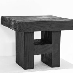 Könnte beinhalten: Ein schwarzer Holzhocker mit quadratischer Oberseite und einem einzigartigen H-förmigen Fuß.