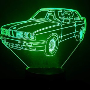 Può includere: Un contorno verde neon di un'auto BMW, con i fari anteriori e posteriori illuminati. L'auto è su una base nera a forma triangolare.