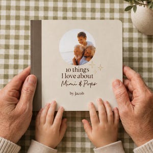 Adult and child holding a personalized grandparents photo board book on a beige gingham background. The cream cover features a circular family photo and a custom “10 Things I Love About Grandparents” title.