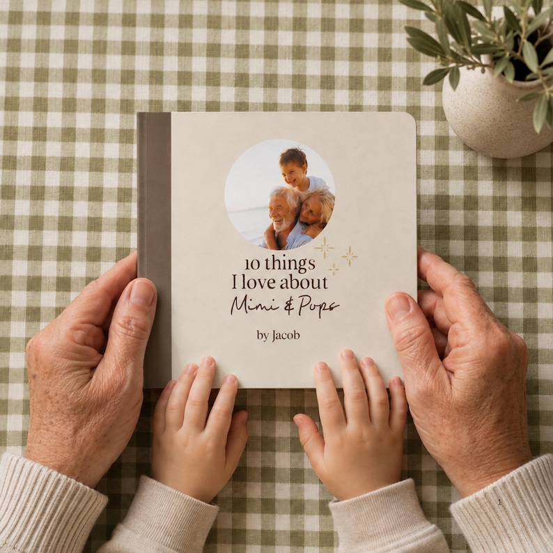 Adult and child holding a personalized grandparents photo board book on a beige gingham background. The cream cover features a circular family photo and a custom “10 Things I Love About Grandparents” title.