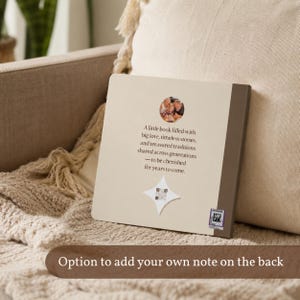 Personalized grandparents photo book back cover displayed on a cream sofa, featuring a small family photograph and dedication. Caption highlights the option to add your own note to the back.