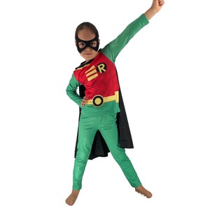 Könnte beinhalten: Ein Kind verkleidet als Robin, ein Superheld aus den Batman-Comics. Das Kostüm ist rot, grün und gelb mit einem schwarzen Umhang und einer schwarzen Maske. Das Kind steht mit einem erhobenen Arm in einer Superheldenpose.