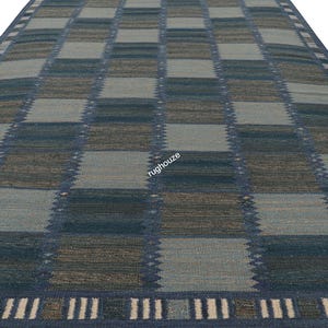 Puede incluir: Una alfombra rectangular con un patr&oacute;n de cuadros en tonos de azul, gris y marr&oacute;n. La alfombra tiene un borde con un dise&ntilde;o geom&eacute;trico repetitivo. La vista en perspectiva resalta la textura y el dise&ntilde;o de la alfombra.